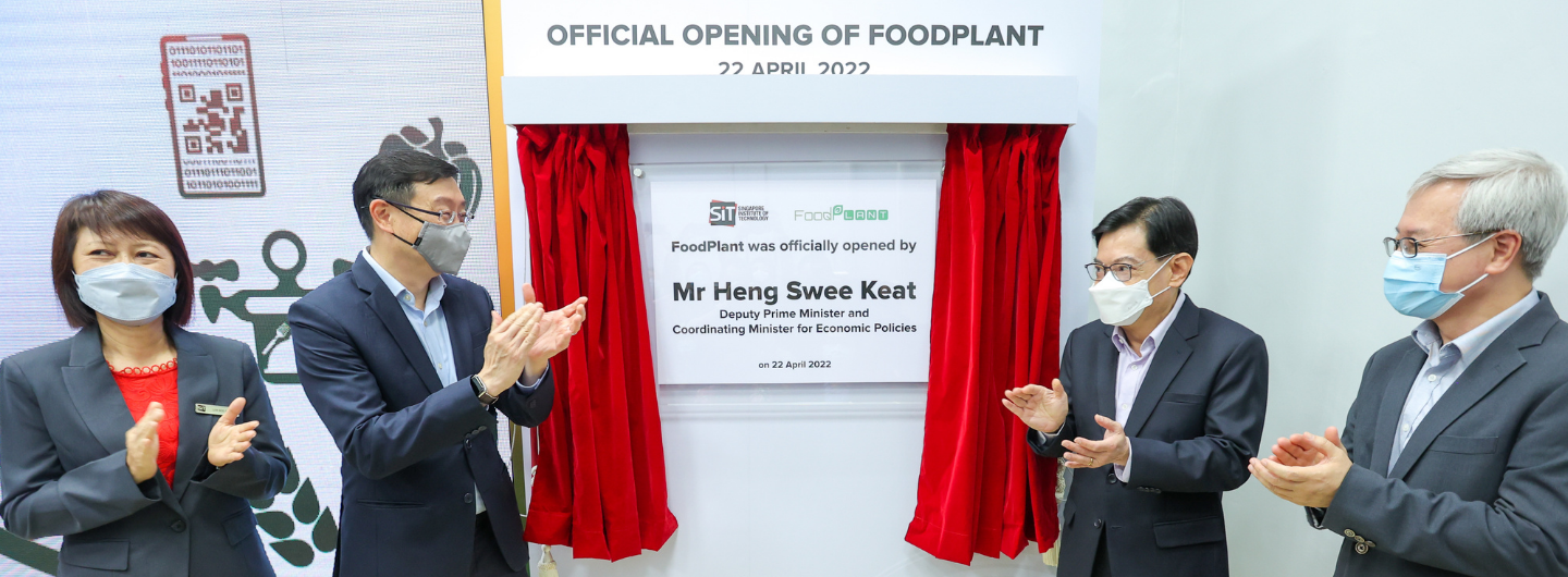 Group of people in suits and masks applauding at "FoodPlant" opening ceremony.